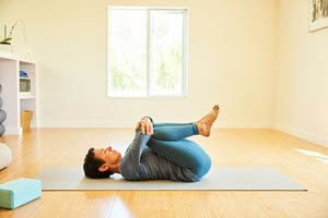 Donna lying supine on her mat with knees drawn to her chest by both forearms 